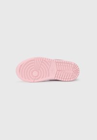 Rosa gummisåle av en Nike sneakers som viser mønstre på sålen, sirkulært grepdesign og preget Nike-logo, isolert på en hvit bakgrunn.