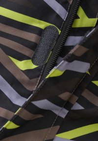 Mönstrad tyg med diagonala ränder i brunt, svart, grått och neongult. Inkluderar en vertikal dragkedja och en texturerad kardborreflik.