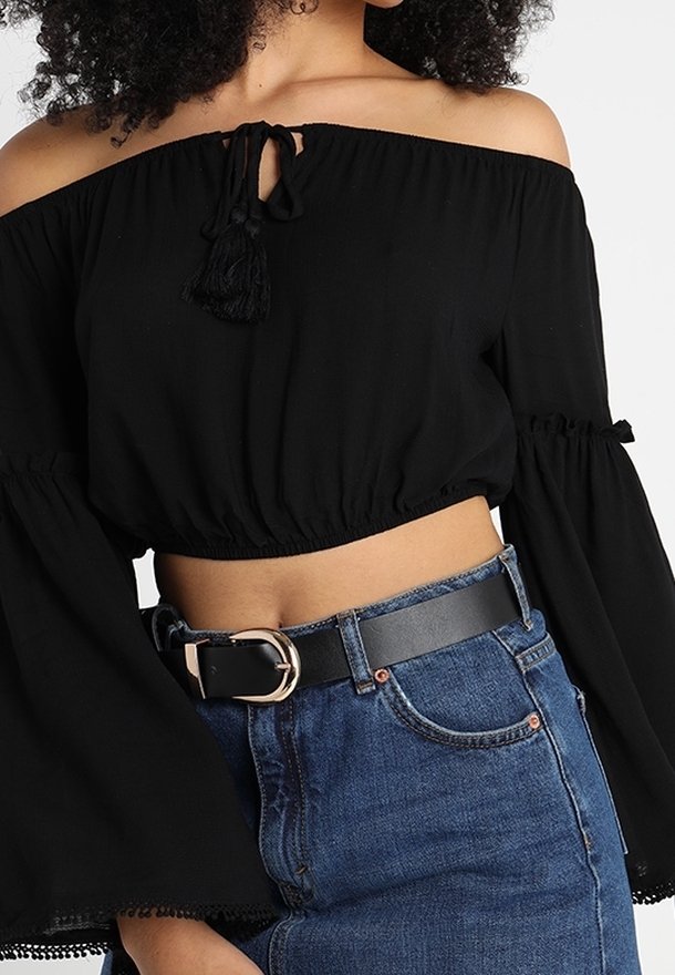 Haut court noir décolleté épaules avec lien à pompons, manches longues évasées et tissu texturé. Assorti à un jean taille haute et une ceinture noire.