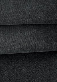 Nahaufnahme von drei gestapelten dunkelgrauen bis schwarzen Jeansstoffstücken mit feiner diagonaler Webstruktur.