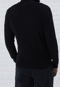 Svartstickad tröja med långa ärmar och ribbad nederkant. Slät textur med en traditionell rundhalsad design, sedd bakifrån.