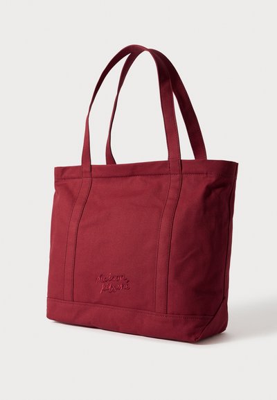 Raudona drobinė rankinė su dviem viršutinėmis rankenomis, dekoruota siūtomis detalėmis ir siuvinėta logotipu priekyje. Plokščias dugno dizainas.