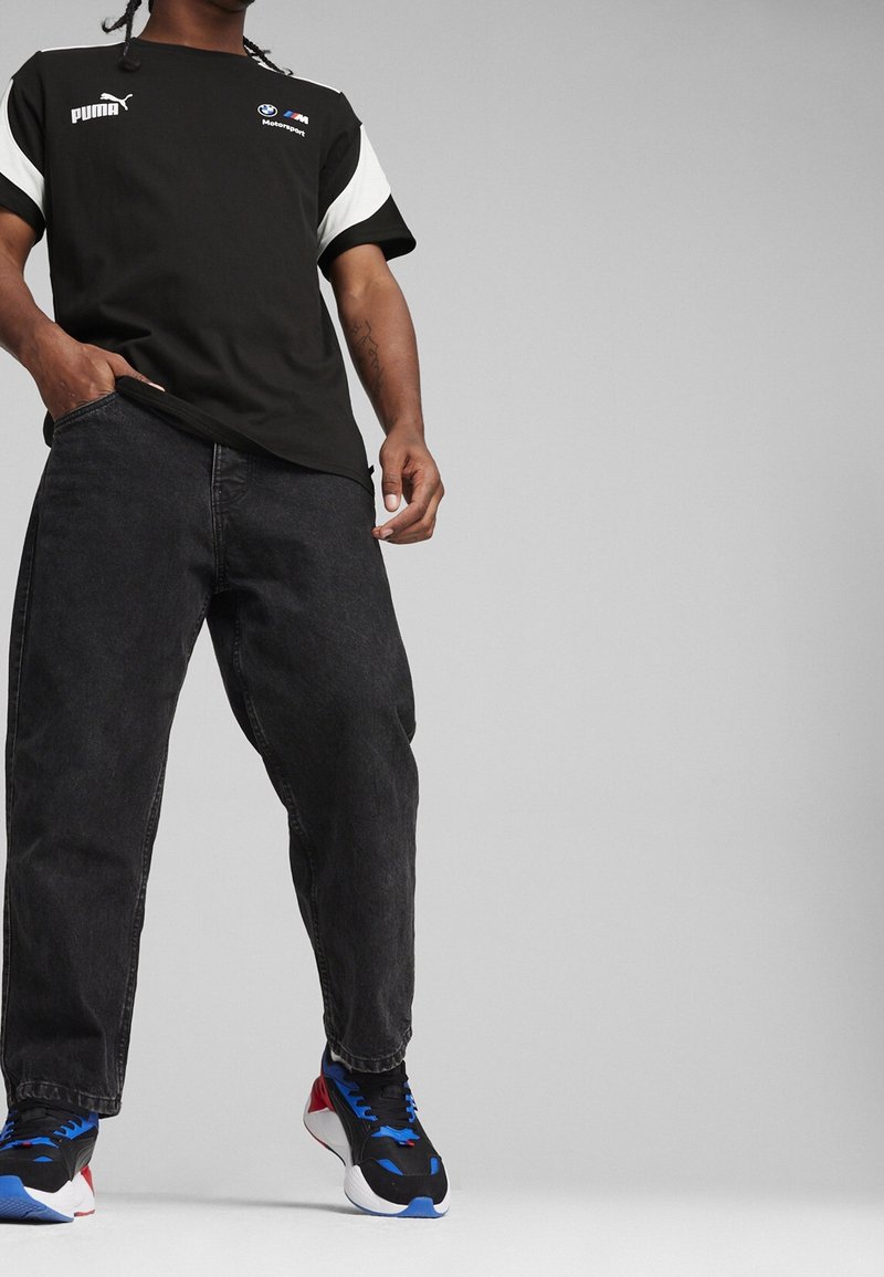 T-shirt nera con accenti bianchi, con i loghi Puma e BMW. Abbinata a jeans neri larghi e sneakers nere con accenti blu e rossi.
