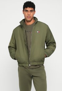 Ανοικτό πράσινο μπουφάν bomber με κλείσιμο φερμουάρ, ελαστικούς καρπούς και μέση. Διαθέτει μια μικρή επένδυση λογότυπου στο στήθος. Λείος υφασμάτινος ιστός.