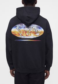 Person wearing black hoodie with colorful world map and air temperature scale printed on the back, facing away.