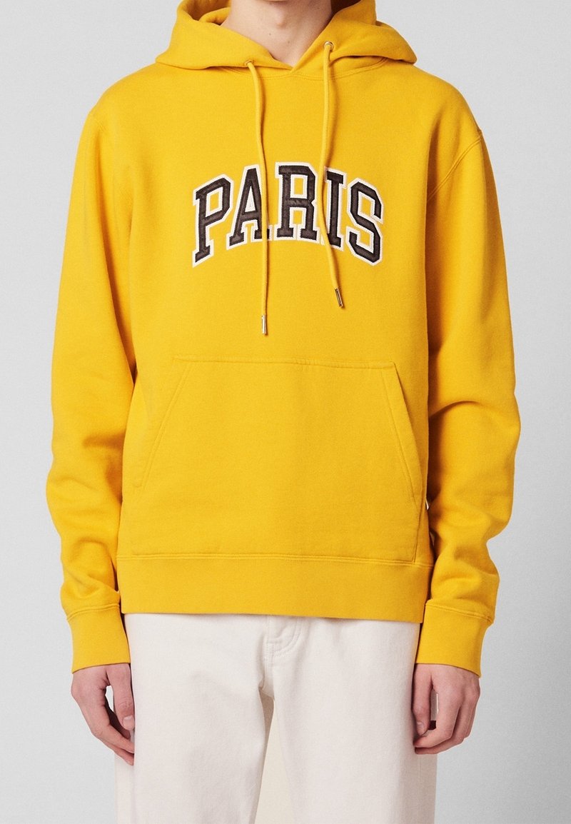 Sweat à capuche jaune avec l'inscription "PARIS" en lettres noires et blanches audacieuses. Il possède une poche avant et des poignets côtelés. Texture lisse.