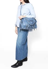 Borsa in denim di colore azzurro chiaro, con doppi manici superiori, tracolla regolabile, chiusura con zip e dettagli in frange.