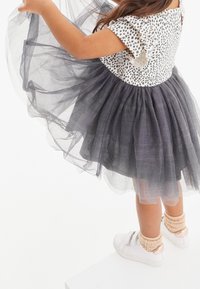 Black and white polka dot top with short ruffled sleeves, paired with a gray tulle skirt. Model wears white sneakers with knitted accents.