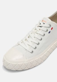 Białe trampki z płótna z gumowym czubkiem i wzorzystą gumową podeszwą. Posiadają otwory na sznurowadła oraz trzy kolorowe akcenty po bokach.