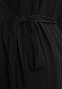 Sort stofkjole med en bundet talje-detail, der har en blød, flydende tekstur og en glat finish. Bæltet er knyttet og strækker sig udad.