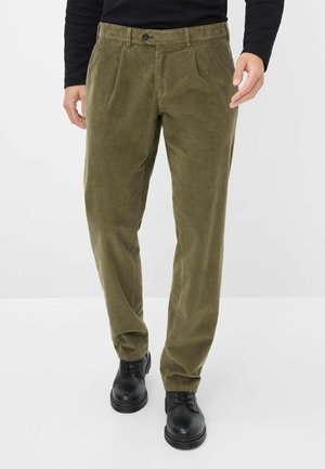 Olijfgroene ribfluwelen broek met plooien aan de voorkant, knoopsluiting en rechte pijpen, gecombineerd met zwarte veterschoenen.