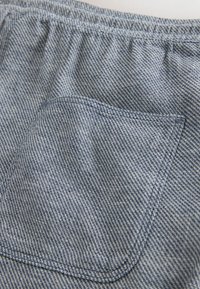 Gros plan sur une poche en tissu gris et blanc texturé avec une couture détaillée sur une ceinture de vêtement.