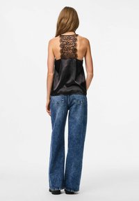 Crna satenasta top haljina s cvjetnim čipkastim detaljem na leđima, u kombinaciji s visokim, širokim plavim trapericama. Glatka tekstura, minimalistički dizajn.