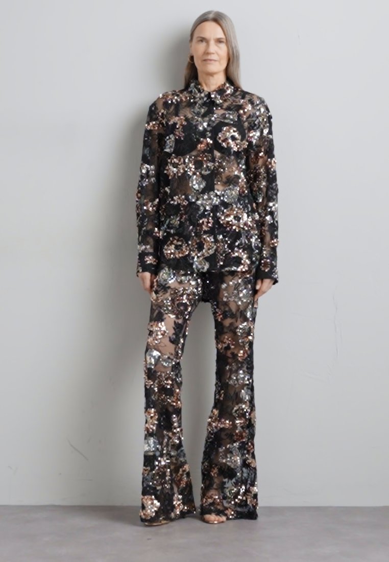 Ensemble noir transparent avec des motifs floraux aux nuances métalliques, comprenant un haut à boutons et un pantalon évasé avec des accents en sequins.