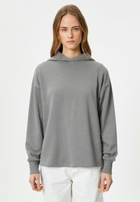 Sudadera gris con capucha, de manga larga, corte relajado, textura suave y puños acanalados. Diseño minimalista sin patrones ni adornos.