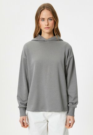 Sudadera gris con capucha, de manga larga, corte relajado, textura suave y puños acanalados. Diseño minimalista sin patrones ni adornos.