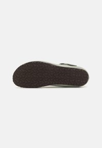 Suela de zapato de goma con un patrón texturizado en forma de olas. La coloración varía de verde claro a marrón oscuro alrededor de los bordes. Diseño plano.