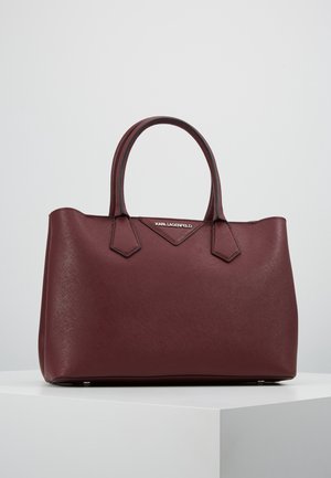 Burgunderrote Leder-Shopper-Tasche mit zwei Griffen und dezentem Strukturmuster, stehend auf einem weißen Podest vor einem schlichten Hintergrund.