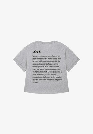 Szürke pamut póló rövid ujjakkal, amelyen a „SZERETET” szó szerepel vastag fekete betűkkel, alatta pedig egy kisebb fekete betűs definíció található.