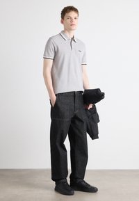 Γκρι πόλο μπλούζα με μαύρες ρίγες στον γιακά, συνδυασμένη με χαλαρά μαύρα τζιν παντελόνια και μαύρα αθλητικά παπούτσια. Το μοντέλο κρατάει μια μαύρη ζακέτα.