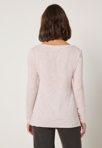Majica dugih rukava u nježno roza boji, s ležernim krojem i okruglim izrezom. Ima glatku teksturu i zaobljeni rub, uparena s tamnim hlačama.