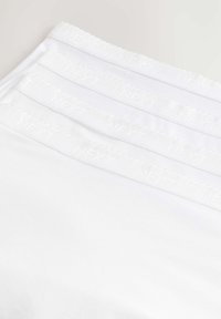 Bílé bavlněné spodní prádlo se širokými elastickými pásky a logem "NEXT". Hladký povrch a bezproblémový design. Více párů naskládáno v záběru.