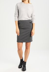 Suéter de punto gris claro con cuello redondo, combinado con una falda entallada de estampado negro y gris que presenta dos botones decorativos. Botines negros.