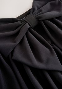 Abito in tessuto nero con un grande fiocco in vita, con morbide pieghe e una texture liscia, che crea un aspetto a strati.