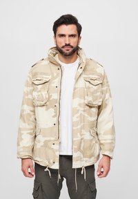 Tarnjacke in Beigetönen, ausgestattet mit einer Kapuze, mehreren Fronttaschen und einem Kordelzugsaum für eine anpassbare Passform.
