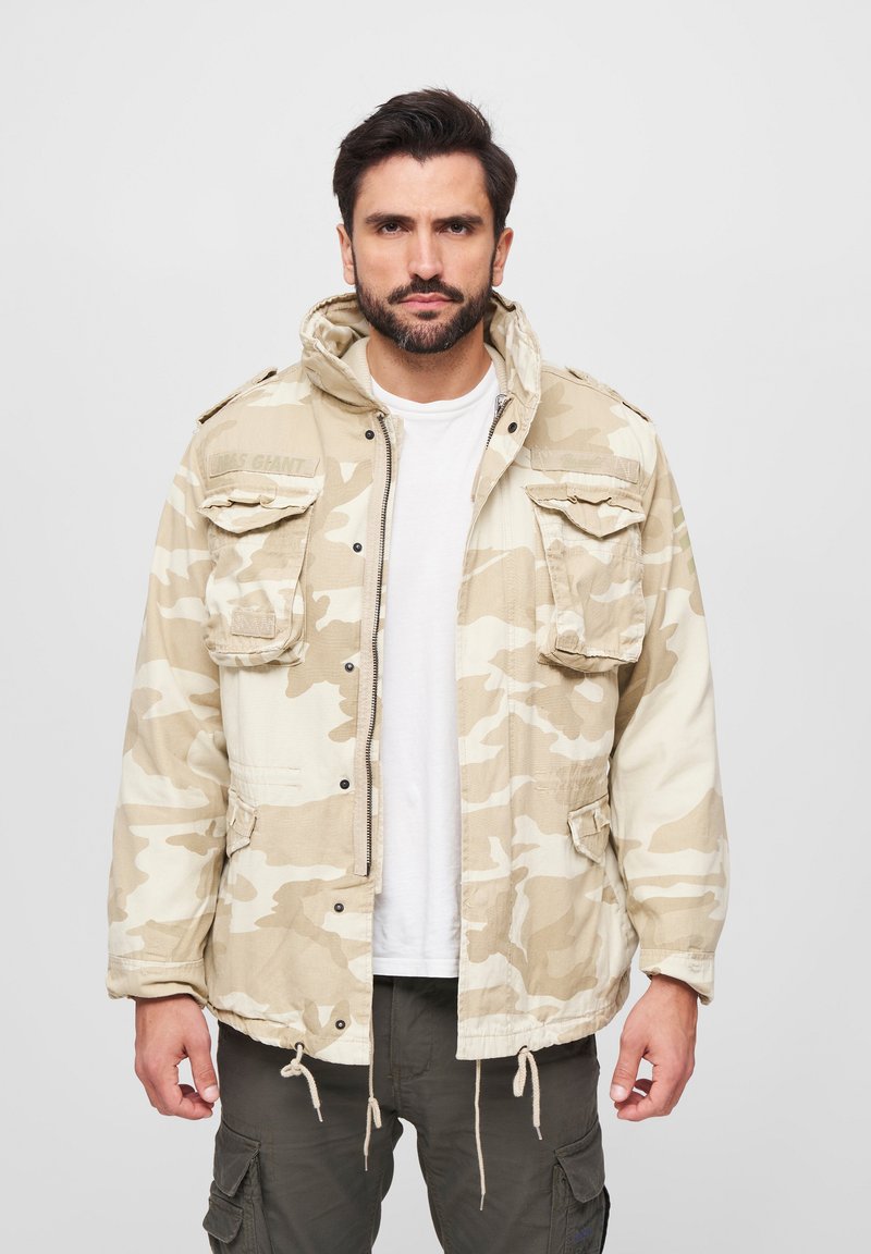 Tarnjacke in Beigetönen, ausgestattet mit einer Kapuze, mehreren Fronttaschen und einem Kordelzugsaum für eine anpassbare Passform.