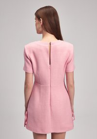 Kurzes rosa Kleid aus strukturiertem Stoff, mit kurzen Ärmeln, einem Reißverschluss hinten und Schleifenakzenten an den Seiten.