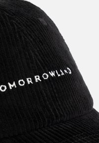 Zwarte corduroy pet met een gebogen rand, met "TOMORROWLAND" in het wit geborduurd op de voorkant. Getextureerde stof met verticale strepen.