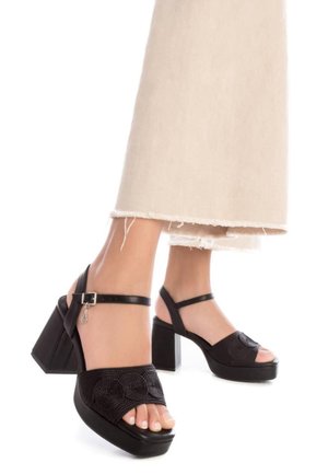 Sandalias de tacón negras con parte superior texturizada, diseño de punta abierta y tacón grueso. Con correa de tobillo con hebilla y acentos florales.