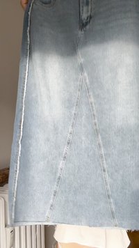 Falda de mezclilla azul claro con corte recto, detalles de costura en ángulo y dobladillo deshilachado. Textura suave con acabado clásico de mezclilla.