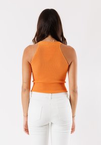Top arancione a coste con un design aderente e un collo alto. Il modello indossa pantaloni bianchi a vita alta. Nessun motivo o accento prominente.