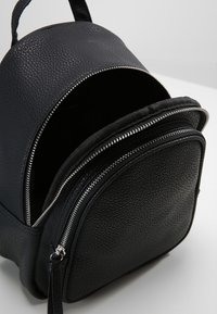 Černý texturovaný kožený batoh kulatého tvaru, s hlavním zipovým prostorem a přední kapsou se stříbrnými zipy.