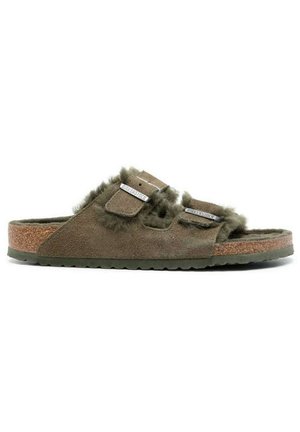Sandali in suede verde oliva con bordo in pelliccia sintetica, due cinturini regolabili e soletta in sughero. Suola in gomma testurizzata per aderenza e comfort.