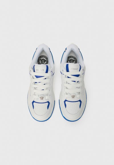 Sneakers bianchi con accenti blu, caratterizzati da un pannello laterale testurizzato, chiusura con lacci e logo Versace sulla linguetta e sulla suola.