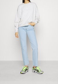Sudadera gris de gran tamaño, jeans rectos de color azul claro y zapatillas negras, blancas y verde neón con acentos estampados.