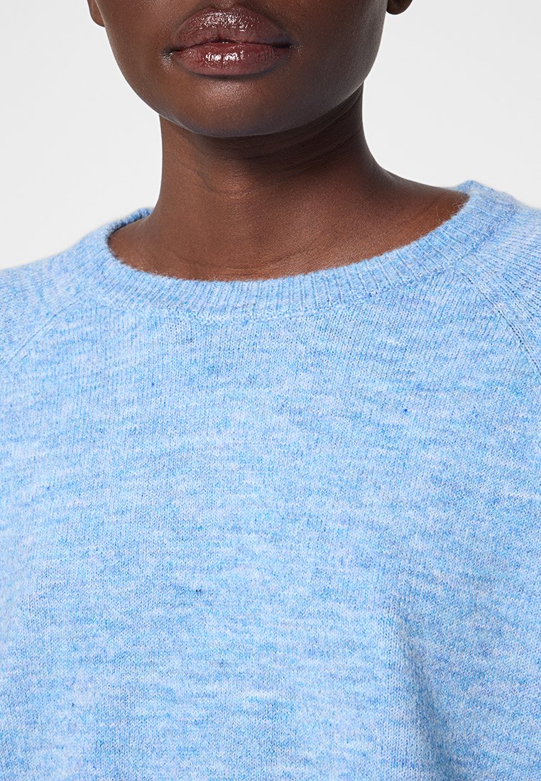Hellblauer gestrickter Pullover mit Rundhalsausschnitt. Weiche Textur, Raglanärmel und subtile Sprenkel in dunklerem Blau durchgehend.