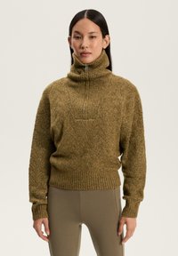 Sweter dziany w oliwkowej zieleni z wysokim kołnierzem, zamknięciem na zamek oraz ściągaczami przy mankietach i dolnej krawędzi. Teksturowany wzór dodaje wizualnego detalu.