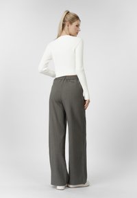 Λευκό μακρυμάνικο ριμπ τοπ με στρογγυλή λαιμόκοψη, σε συνδυασμό με γκρι παντελόνι με φαρδιά μπατζάκια και λευκά παπούτσια, εμφανίζεται από πίσω.