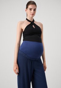 Haut de maternité, design halter noir avec un trou clé, associé à un pantalon large bleu marine en tissu texturé et à taille élastique.