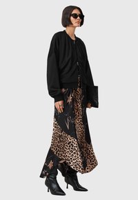 Crna bomber jakna preko maksi haljine s leopard printom i cvjetnim detaljima. Uparena s crnim cipelama na visoku petu s oštrim vrhom i velikim sunčanim naočalama.