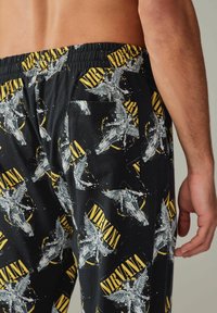 Fekete pamut pizsama nadrág, sárga és fehér Nirvana grafikai mintával, rugalmas derékpánttal és hátsó zsebbel.