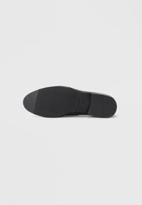 Semelle de chaussure en cuir noir avec une texture lisse, une forme arrondie et un talon en caoutchouc. Présente une marque subtile et un design minimal.