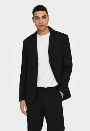 Black blazer made of smooth fabric, single-button design, tailored fit, with a chest pocket and subtle stitching details. Worn over a white t-shirt.