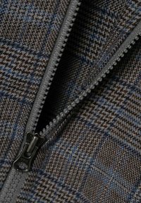 Brunt och blått hundtandsmönstrat tyg med en grå dragkedja, som visar en närbild av textur och mönsterdetaljer.