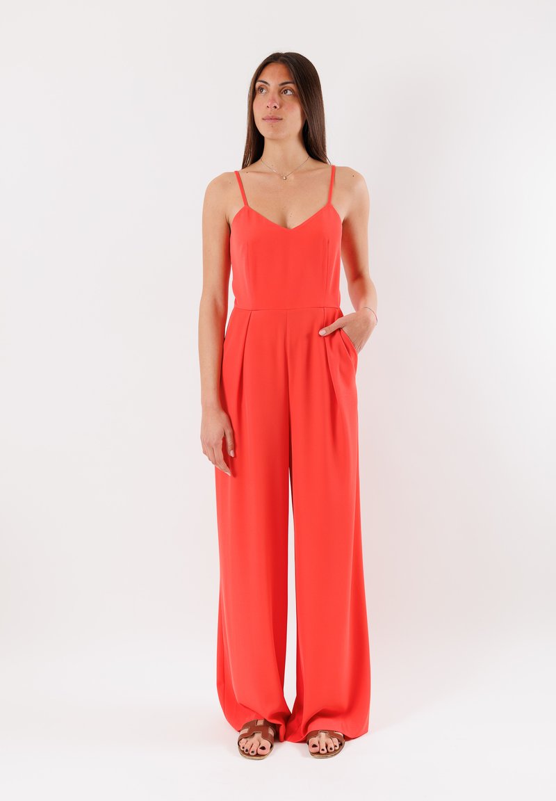 Tuta rossa con corpino aderente, spalline adjustable e pantaloni a gamba larga; presenta tasche laterali e una texture del tessuto liscia.