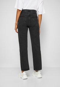 Pantalones vaqueros negros de cintura alta con pierna recta, que cuentan con dos bolsillos traseros y un dobladillo deshilachado, combinados con zapatillas blancas.